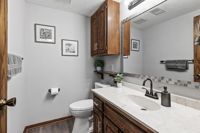 half bath with a textured ceiling, toilet, wood finished floors, vanity, and baseboards