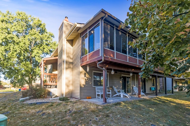 rear view of house with a sunroom, a lawn, a chimney, and a patio