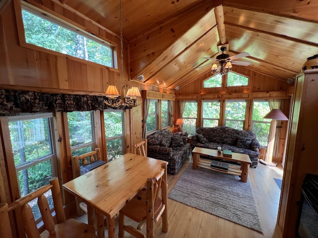 dining area with ceiling fan with notable chandelier, wooden walls, light wood-type flooring, and vaulted ceiling