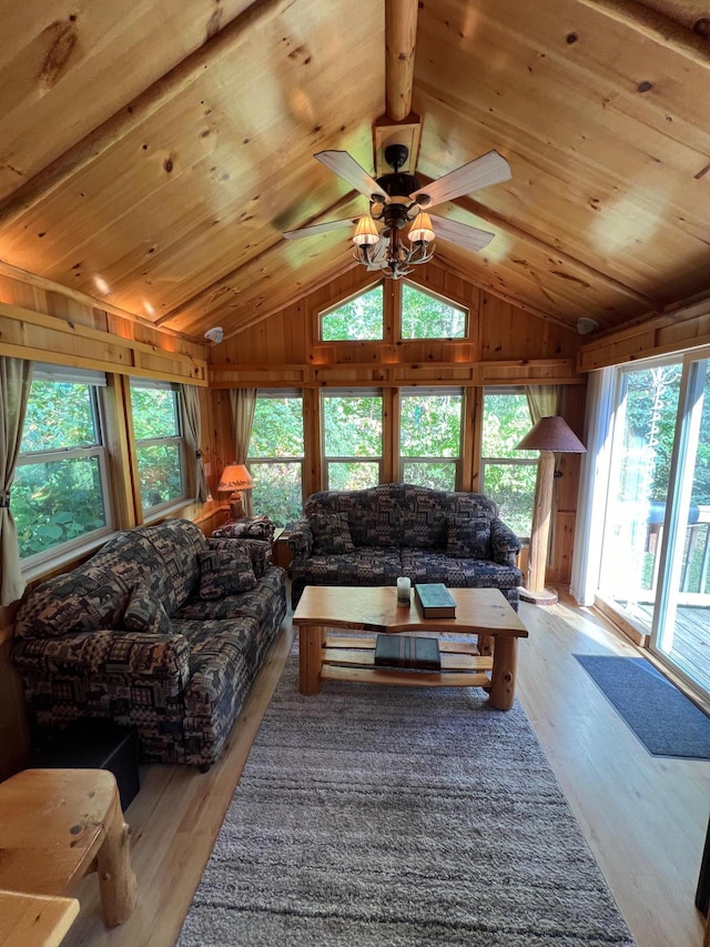 living room featuring ceiling fan, wood walls, lofted ceiling with beams, wooden ceiling, and light hardwood / wood-style floors