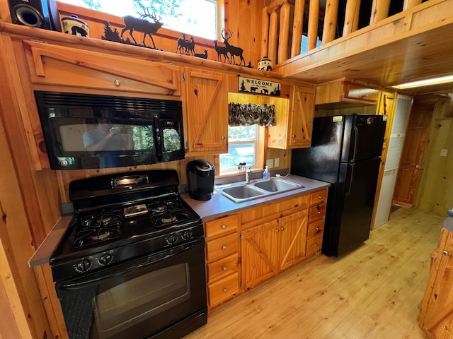 kitchen with black appliances, light hardwood / wood-style floors, wood walls, and sink