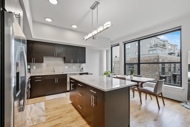 kitchen featuring decorative light fixtures, appliances with stainless steel finishes, a center island, light hardwood / wood-style floors, and decorative backsplash