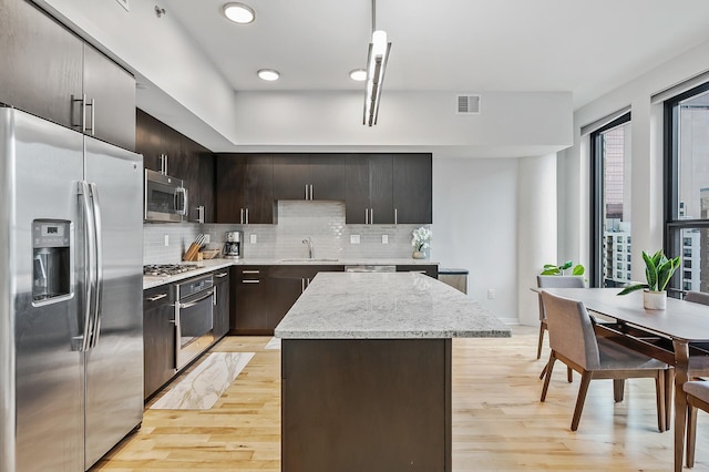 kitchen featuring backsplash, a kitchen island, stainless steel appliances, dark brown cabinets, and light hardwood / wood-style flooring