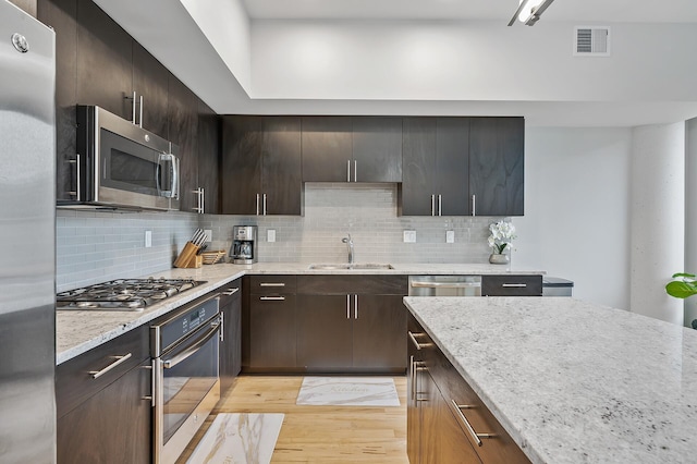 kitchen featuring dark brown cabinets, light hardwood / wood-style floors, sink, appliances with stainless steel finishes, and light stone countertops