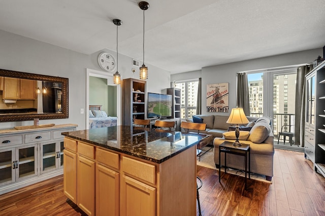 kitchen featuring hanging light fixtures, a kitchen island, a textured ceiling, dark wood-type flooring, and dark stone counters