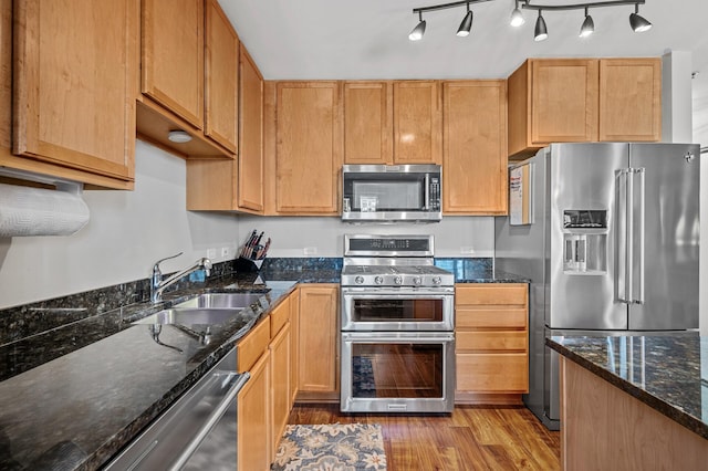 kitchen featuring light hardwood / wood-style flooring, dark stone countertops, appliances with stainless steel finishes, and sink