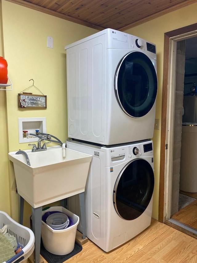 clothes washing area with ornamental molding, light hardwood / wood-style floors, wooden ceiling, and stacked washing maching and dryer