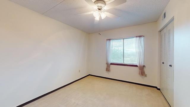 empty room with ceiling fan, light colored carpet, and a textured ceiling