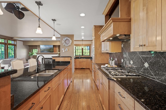 kitchen with light hardwood / wood-style floors, dark stone counters, sink, custom exhaust hood, and hanging light fixtures