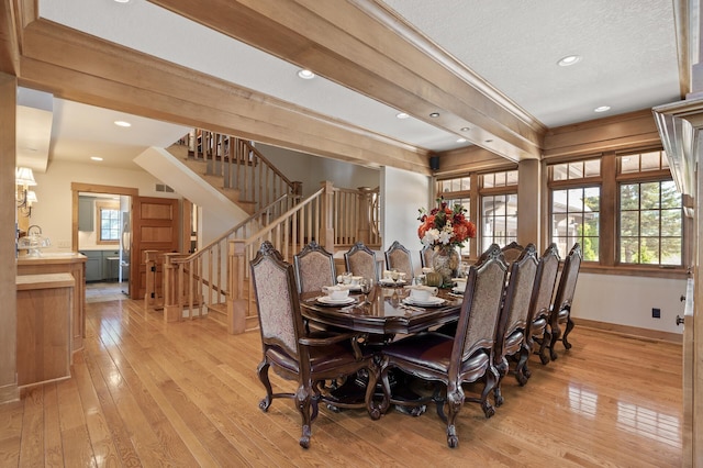 dining area with ornamental molding, beam ceiling, a textured ceiling, and light hardwood / wood-style flooring