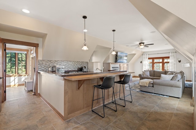 kitchen featuring ceiling fan, kitchen peninsula, decorative light fixtures, backsplash, and a breakfast bar