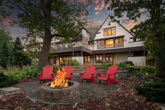 back house at dusk featuring a fire pit, a balcony, and a patio area