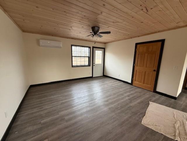 unfurnished room featuring a wall unit AC, wood finished floors, baseboards, and wooden ceiling