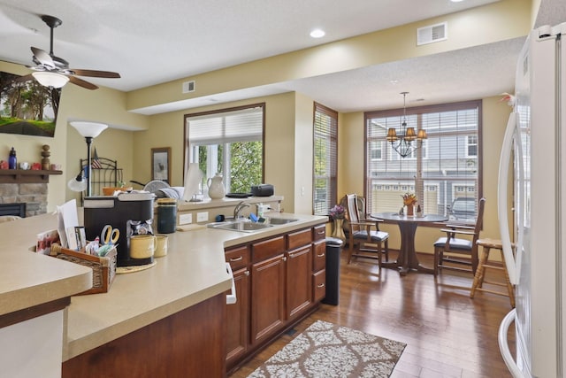 kitchen with dark wood-type flooring, a fireplace, pendant lighting, white fridge, and sink