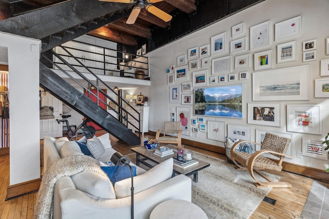 living room with hardwood / wood-style floors, ceiling fan, beam ceiling, and a towering ceiling