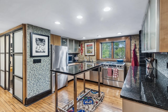 kitchen with tasteful backsplash, stainless steel appliances, sink, dark stone countertops, and light hardwood / wood-style floors