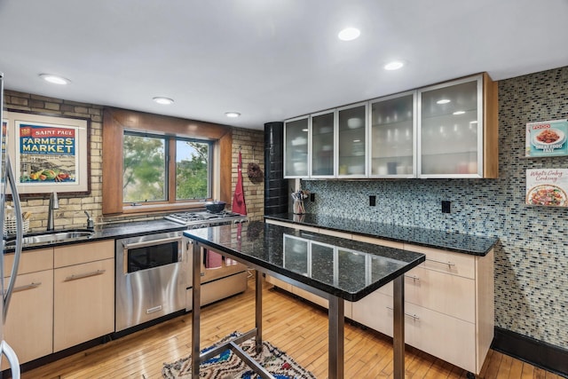 kitchen with sink, dishwasher, backsplash, dark stone countertops, and light wood-type flooring