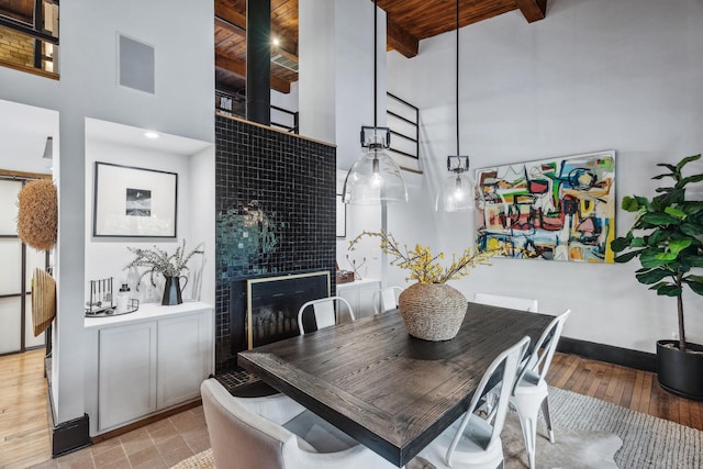 dining area with beam ceiling, a high ceiling, light hardwood / wood-style flooring, a tiled fireplace, and wood ceiling