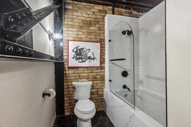 bathroom featuring toilet, tiled shower / bath combo, tile patterned floors, and brick wall