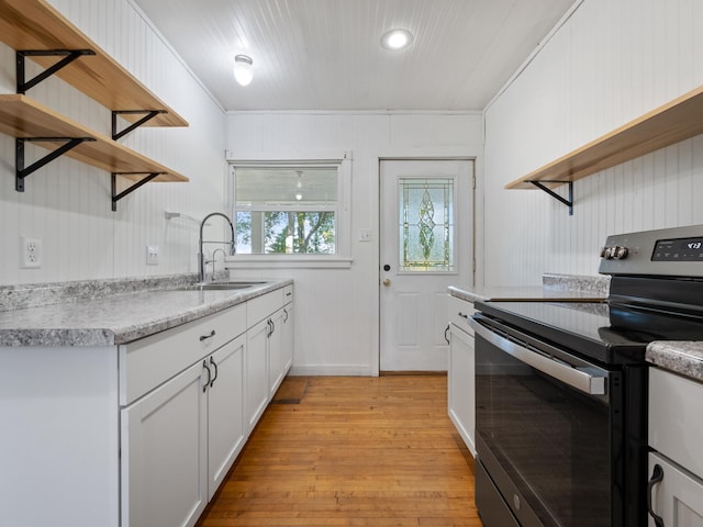 kitchen with wood walls, white cabinets, crown molding, electric range, and light hardwood / wood-style floors