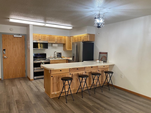 kitchen with stainless steel appliances, a peninsula, a sink, light countertops, and dark wood finished floors