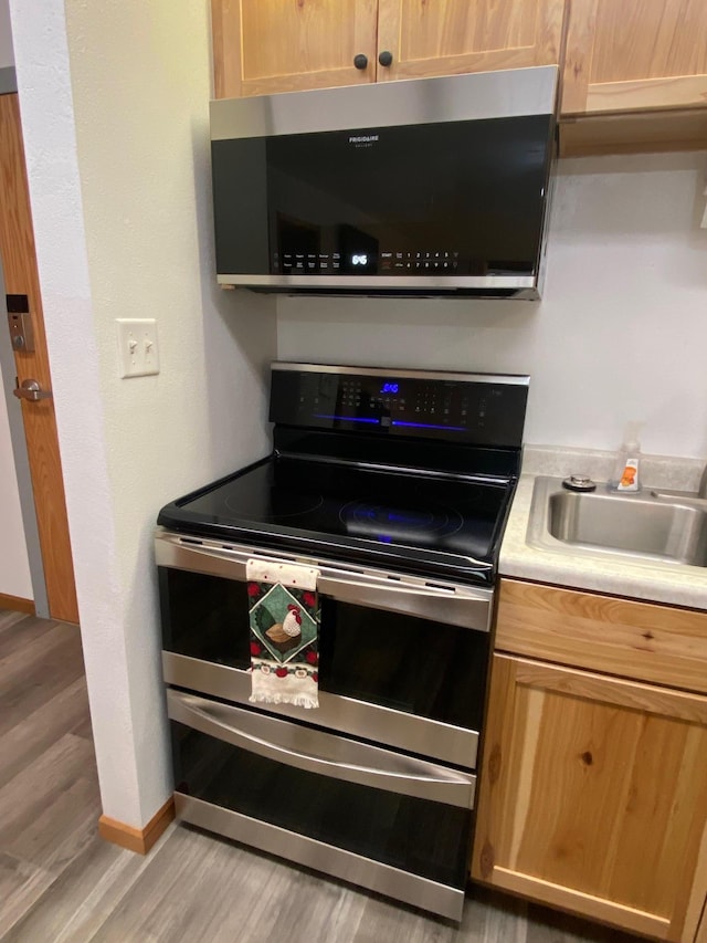 kitchen featuring light countertops, appliances with stainless steel finishes, light wood-style floors, a sink, and baseboards