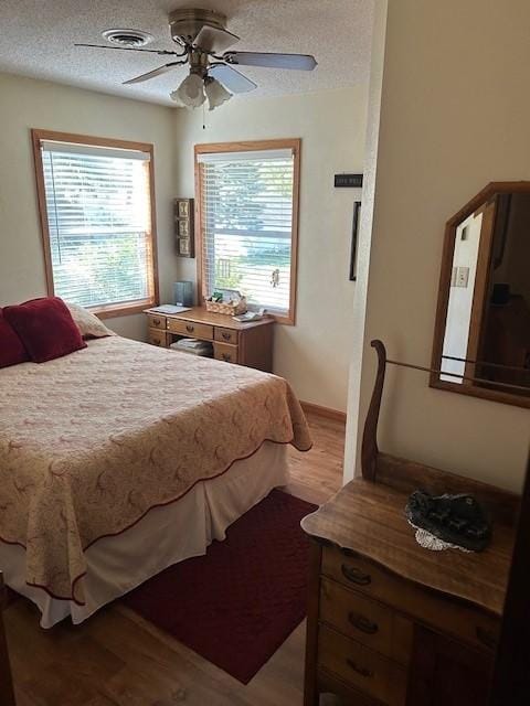 bedroom with ceiling fan, a textured ceiling, multiple windows, and hardwood / wood-style floors