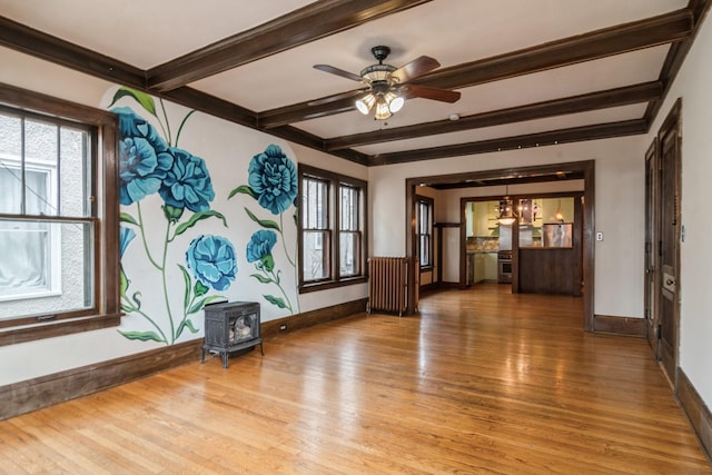 empty room featuring beam ceiling, a wood stove, a wealth of natural light, and hardwood / wood-style floors