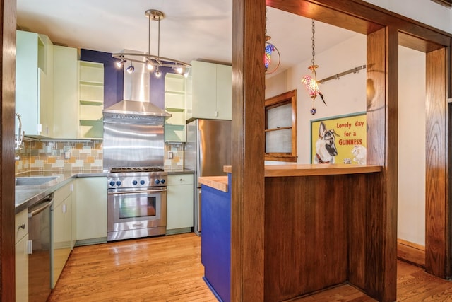 kitchen with backsplash, stainless steel appliances, wall chimney range hood, light hardwood / wood-style flooring, and hanging light fixtures