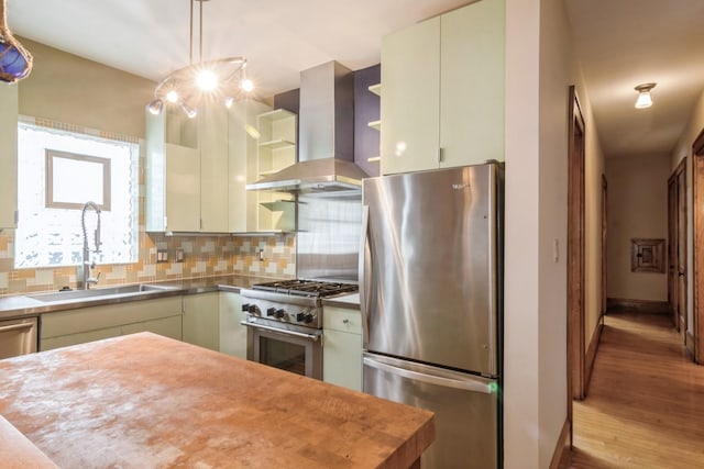 kitchen with wall chimney range hood, sink, hanging light fixtures, decorative backsplash, and stainless steel appliances