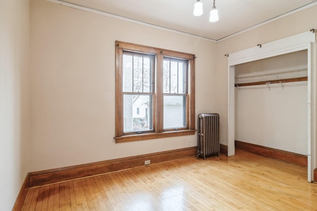 unfurnished bedroom featuring light wood-type flooring, radiator heating unit, crown molding, and a closet