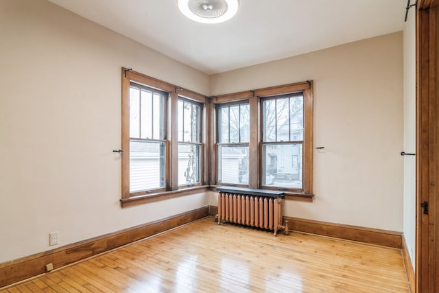 unfurnished room with radiator heating unit, plenty of natural light, and light hardwood / wood-style flooring