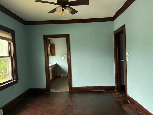 unfurnished bedroom featuring multiple windows, ornamental molding, ensuite bath, and ceiling fan