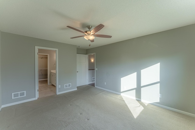 unfurnished bedroom with a spacious closet, light carpet, a closet, and ceiling fan