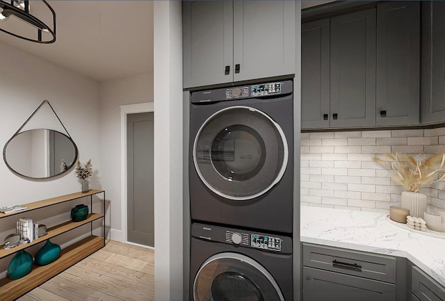 laundry room with stacked washer and clothes dryer, cabinets, and light hardwood / wood-style floors