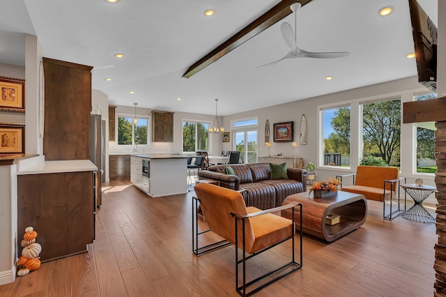 living room featuring light hardwood / wood-style flooring, vaulted ceiling with beams, and ceiling fan with notable chandelier