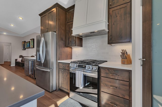 kitchen with dark wood-type flooring, stainless steel appliances, tasteful backsplash, custom range hood, and dark brown cabinets