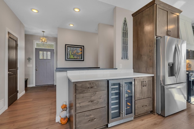 kitchen with light hardwood / wood-style flooring, range, stainless steel fridge, pendant lighting, and wine cooler