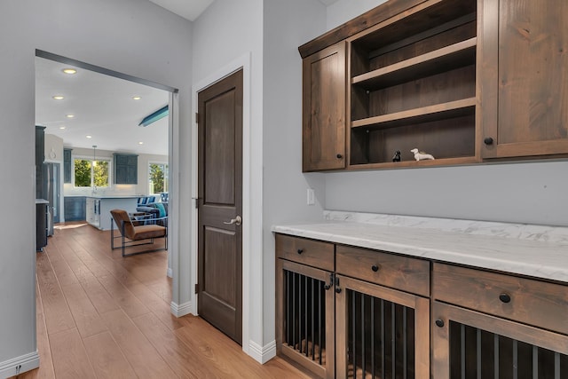 bar featuring stainless steel refrigerator, dark brown cabinetry, light wood-type flooring, and light stone countertops