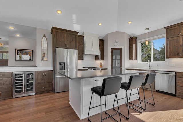 kitchen with hanging light fixtures, a kitchen island, custom range hood, stainless steel appliances, and beverage cooler