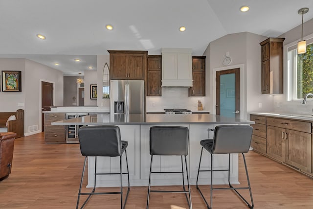 kitchen featuring stainless steel fridge with ice dispenser, decorative light fixtures, premium range hood, and a kitchen island