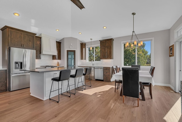 kitchen with appliances with stainless steel finishes, hanging light fixtures, a kitchen island, custom exhaust hood, and light wood-type flooring