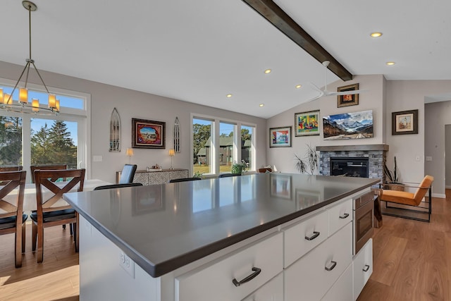 kitchen featuring light hardwood / wood-style flooring, stainless steel microwave, lofted ceiling with beams, white cabinets, and a stone fireplace