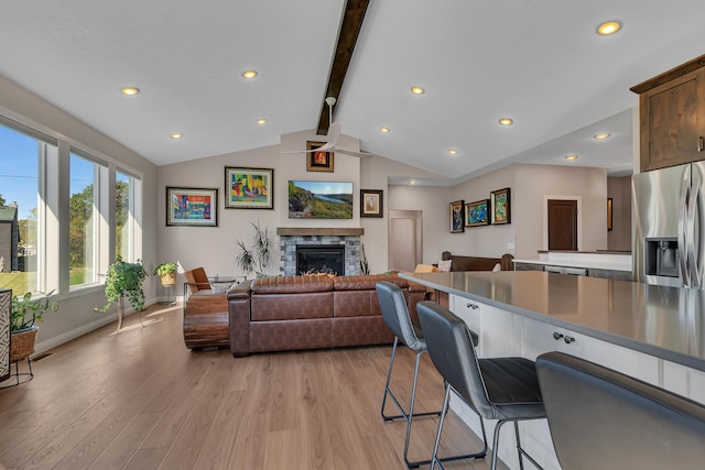 living room with vaulted ceiling with beams, a stone fireplace, and light hardwood / wood-style flooring