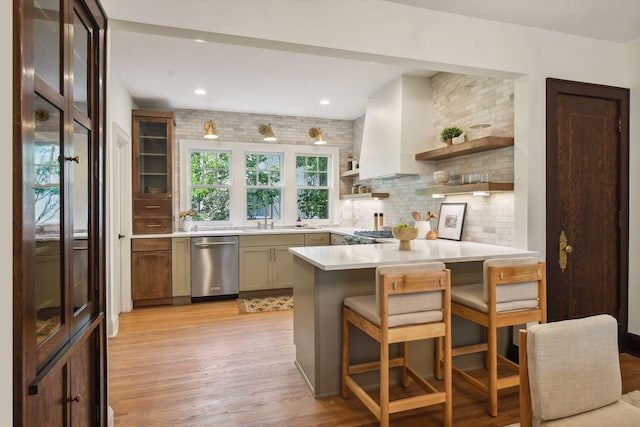 kitchen featuring light wood-type flooring, dishwasher, tasteful backsplash, kitchen peninsula, and a kitchen breakfast bar