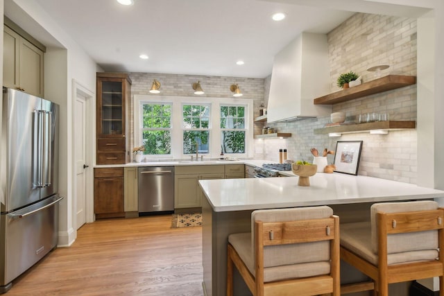 kitchen with tasteful backsplash, a breakfast bar area, kitchen peninsula, light hardwood / wood-style flooring, and appliances with stainless steel finishes