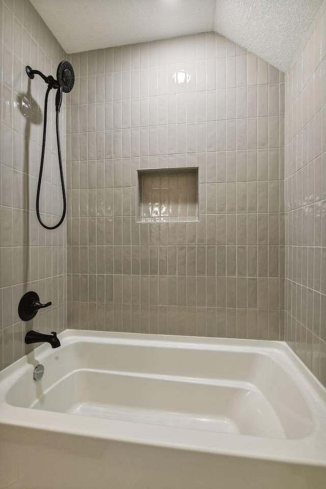 bathroom with a textured ceiling, lofted ceiling, and tiled shower / bath combo