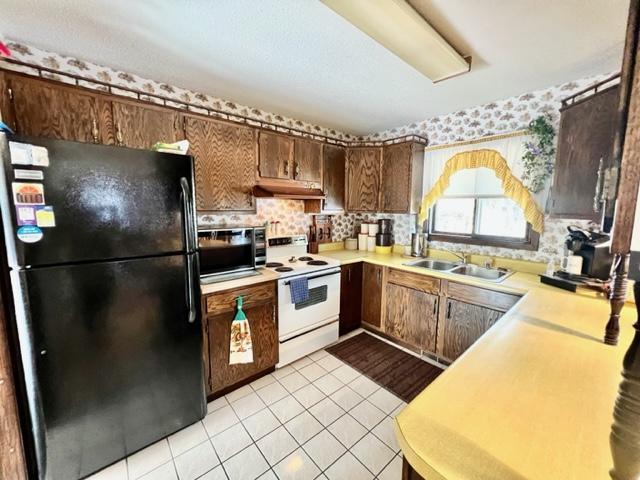 kitchen with black fridge, light tile patterned flooring, sink, white range with electric stovetop, and decorative backsplash