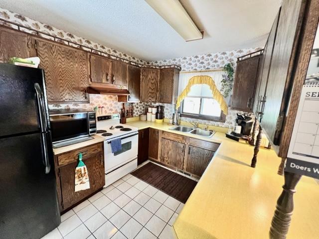 kitchen with sink, backsplash, light tile patterned floors, white range with electric stovetop, and black refrigerator