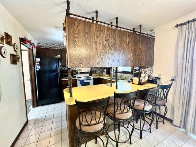 kitchen featuring light tile patterned flooring, kitchen peninsula, a textured ceiling, electric stove, and black refrigerator